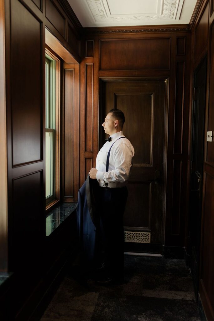 Groom getting ready in front of window at Bottleworks hotel in Indianapolis.