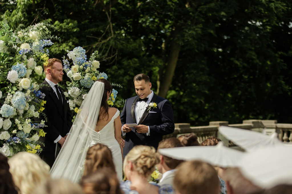 Bride reading vows to his groom during the ceremony at newfields, grooms reaction.