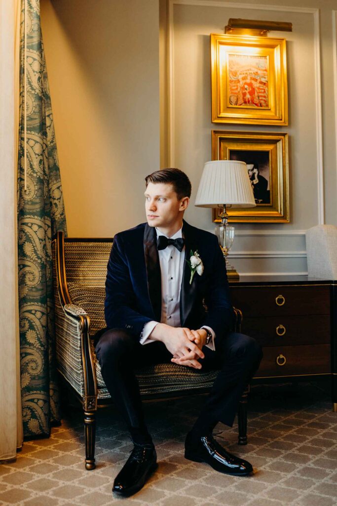 Groom sitting in French style chair in groom suite.