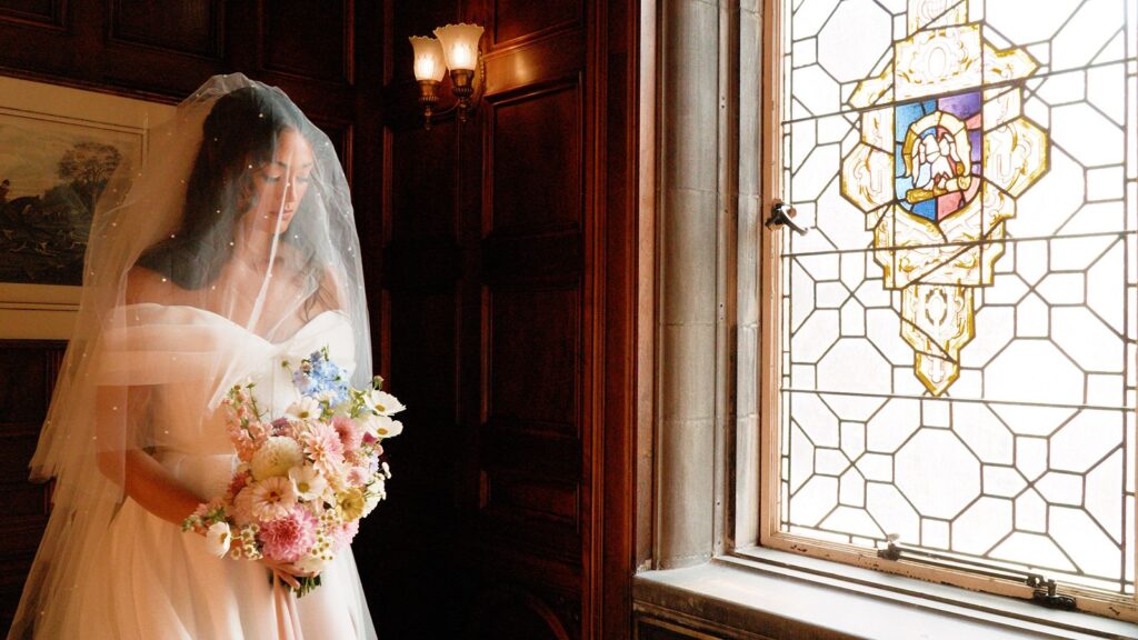 Bride holding soft colorful wedding bouquet type near window.
