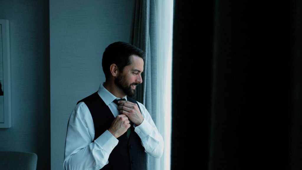 Groom getting ready for first look before wedding ceremony by window.